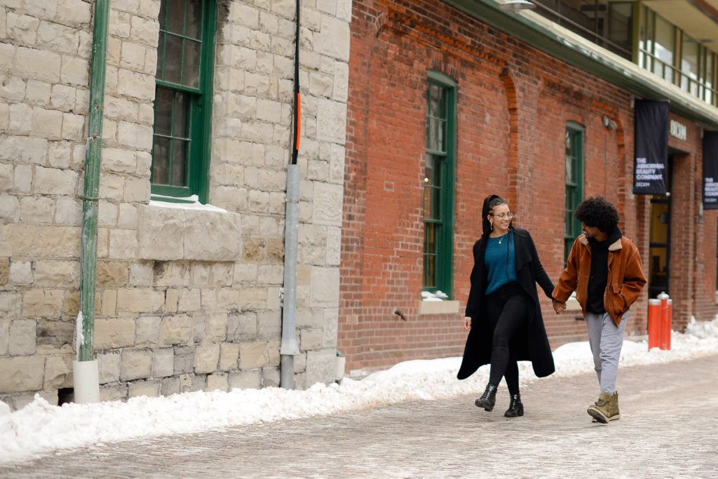 couple holding hands in snow covered street in toronto for an engagement photoshoot