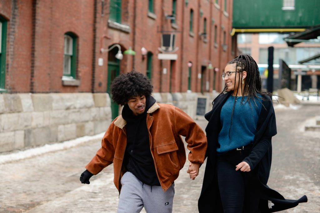 couple in winter coats holding hands and laughing at engagement photoshoot