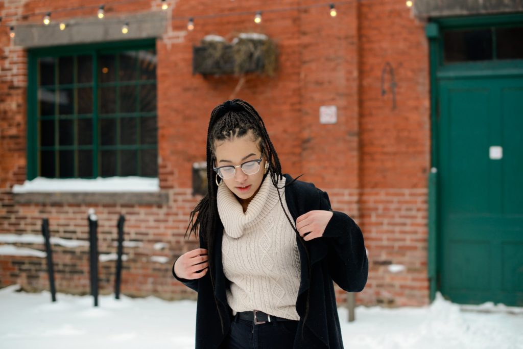 woman in glasses and coat in front of red brick wall