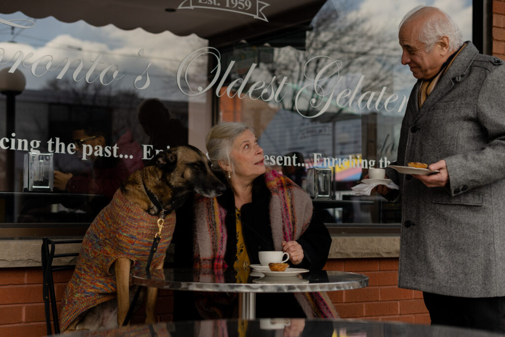 Tudy Weiss sits outside of the bakery with dog and says hello to Gerry Mendicino in a scene from T.A.R.T