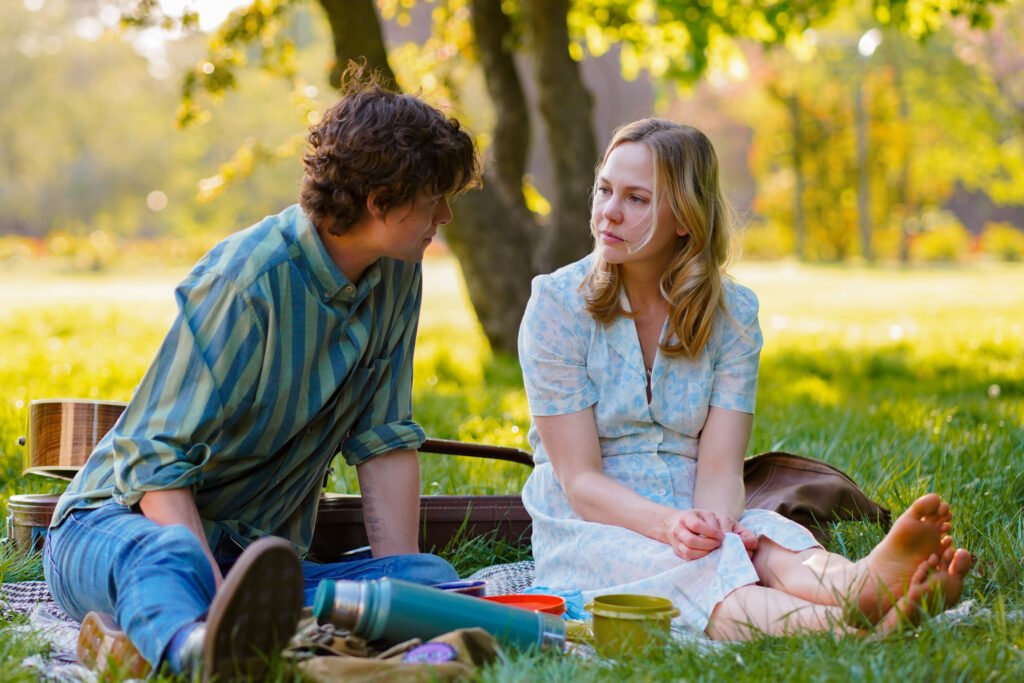 Adelaide Clemens sits having a picnic with Douglas Smith in a park in a scene from The Swearing Jar