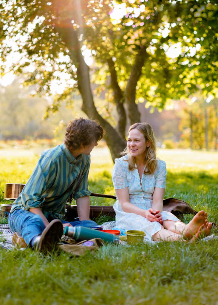 Adelaide Clemens sits having a picnic with Douglas Smith in a park in a scene from The Swearing Jar