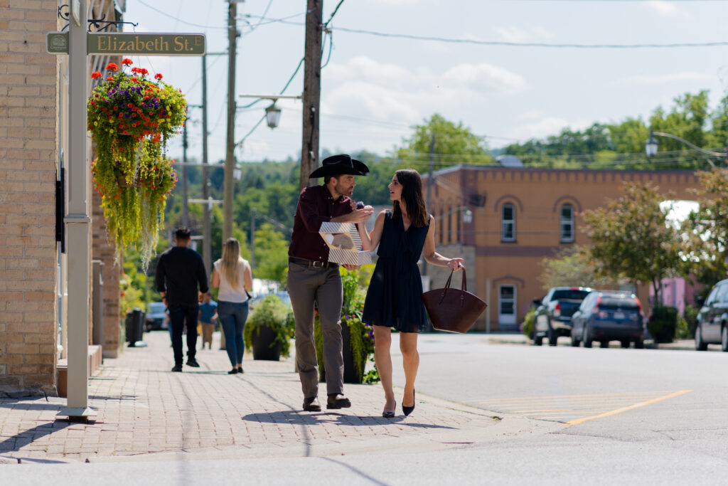 Nola Martin and Tim Rozon walk together through small town feeding each other cupcakes in Love in Wolf Creek, a Hallmark movie