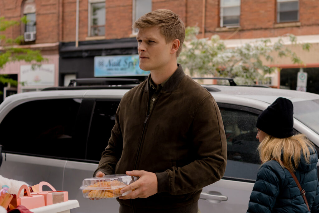 Adrian Spencer holds cupcakes outside store in Hallmark movie, Christmas Lucky Charm