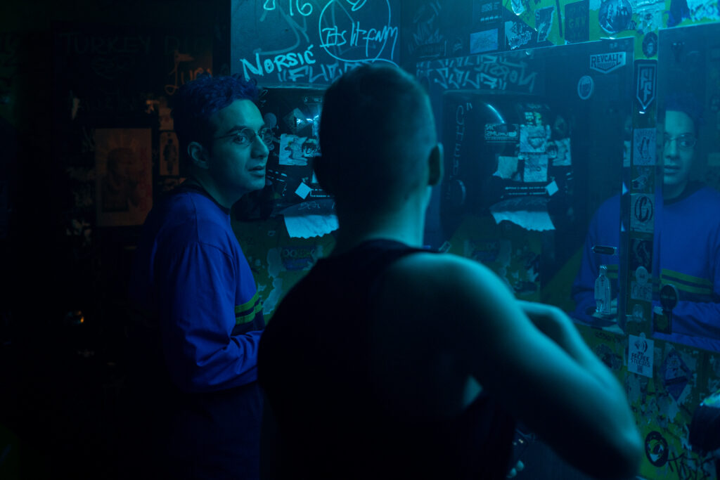 Bobby Summers speaks to a topless man in the bathroom of a nightclub in a scene from I Hate People, People Hate Me