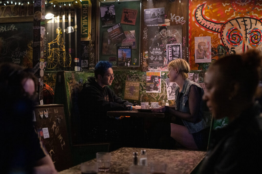 Bobby Summers talks with a friend in a bar booth in a scene from I Hate People, People Hate Me