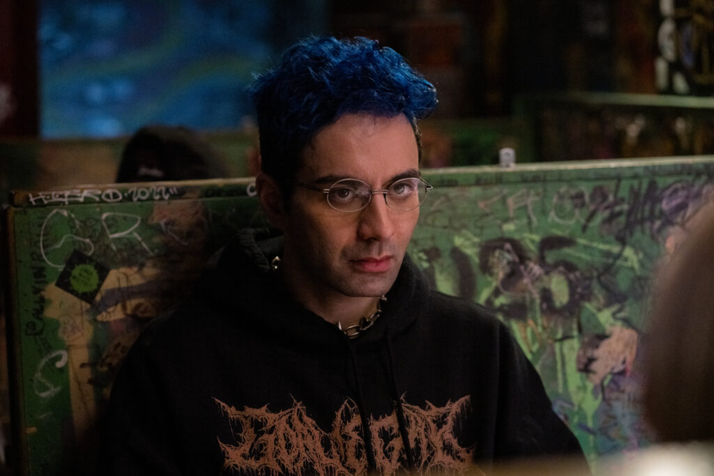 Bobby Summers sits in a booth in a bar and looks confused in a scene from I Hate People, People Hate Me