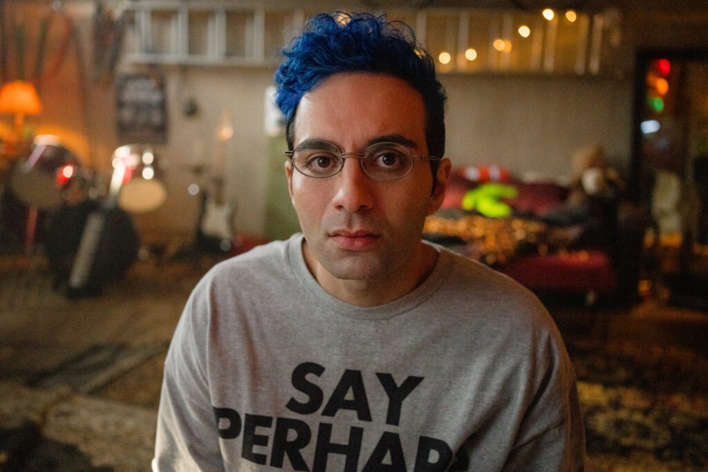 Bobby Summers looks straight to camera with blue hair, in his bedroom in a scene from I Hate People, People Hate Me