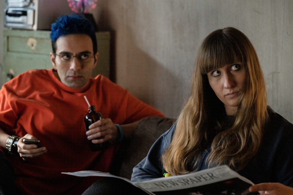 Bobby Summers and Lily Kazimiera looks judgementally from where they are sitting on a coach in a scene from I Hate People, People Hate Me