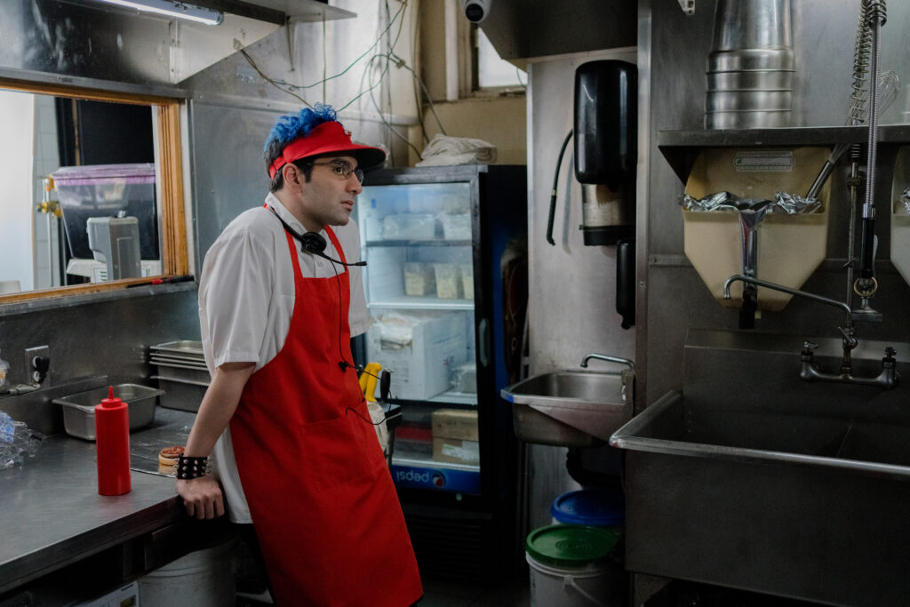 Bobby Summers in his fast food outfit leans in the kitchen in a scene from I Hate People, People Hate Me