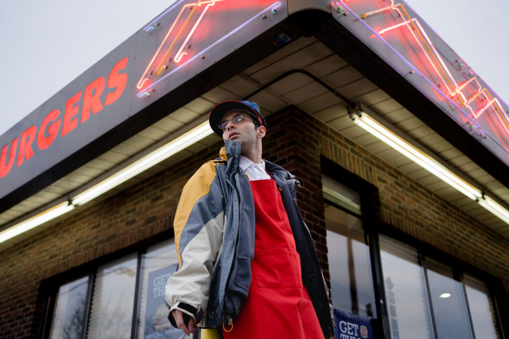 Bobby Summers wears his fast food outfit outside while smoking in a scene from I Hate People, People Hate Me