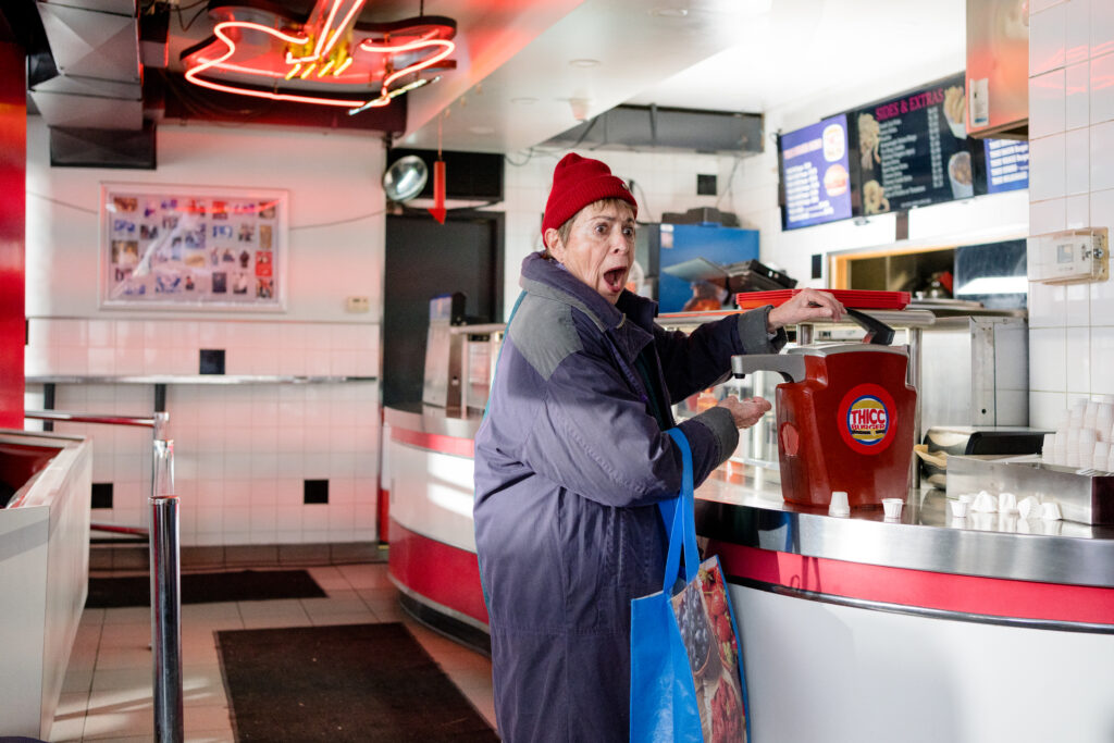 A customer in the burger joint looks shocked as she gets some ketchup in a scene from I Hate People, People Hate Me