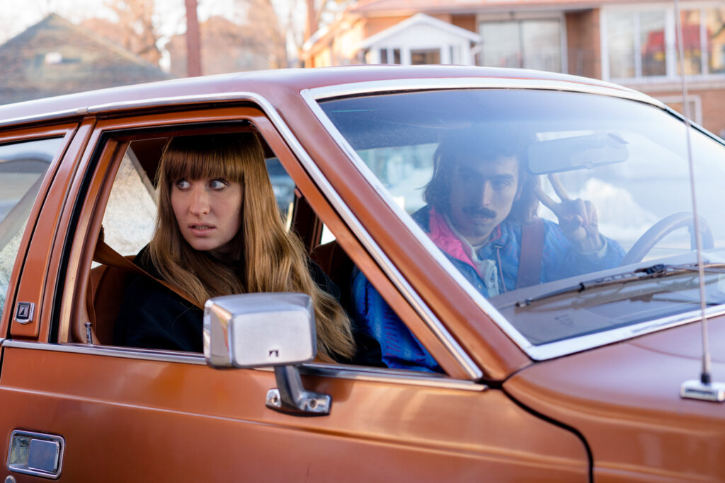 Lilly Kazimiera sits in the passenger seat of an old brown car in a scene from I Hate People, People Hate Me