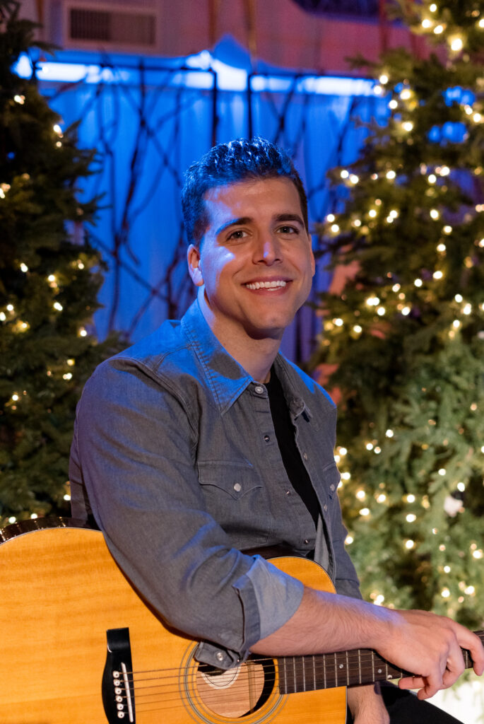 David Pinard looks straight to camera with guitar in hand for stills photographer, Lauren Newman on-set of Country Hearts Christmas