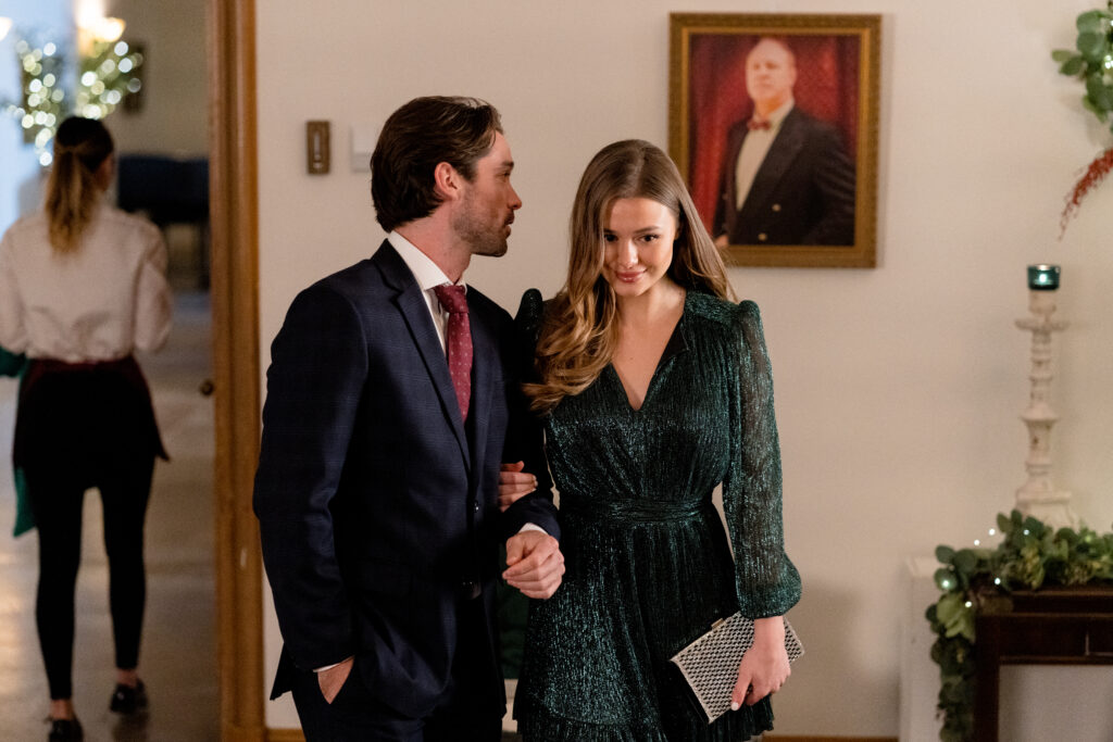 Celeste Desjardins and Joe Scarpellino walk arm in arm laughing and talking in a scene from the Hallmark movie Christmas with the Knightlys