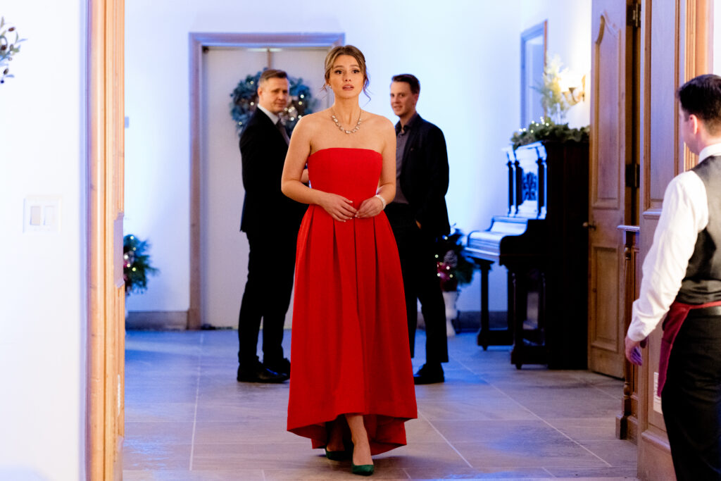 Celeste Desjardins walks into a party with a red evening gown in a scene from the Hallmark movie Christmas with the Knightlys