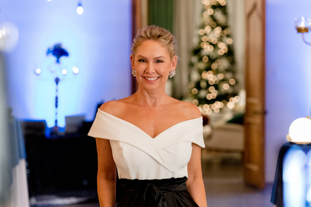 Kym Johnson Herjavec smiles to camera in a black and white evening gown in a scene from the Hallmark movie Christmas with the Knightlys