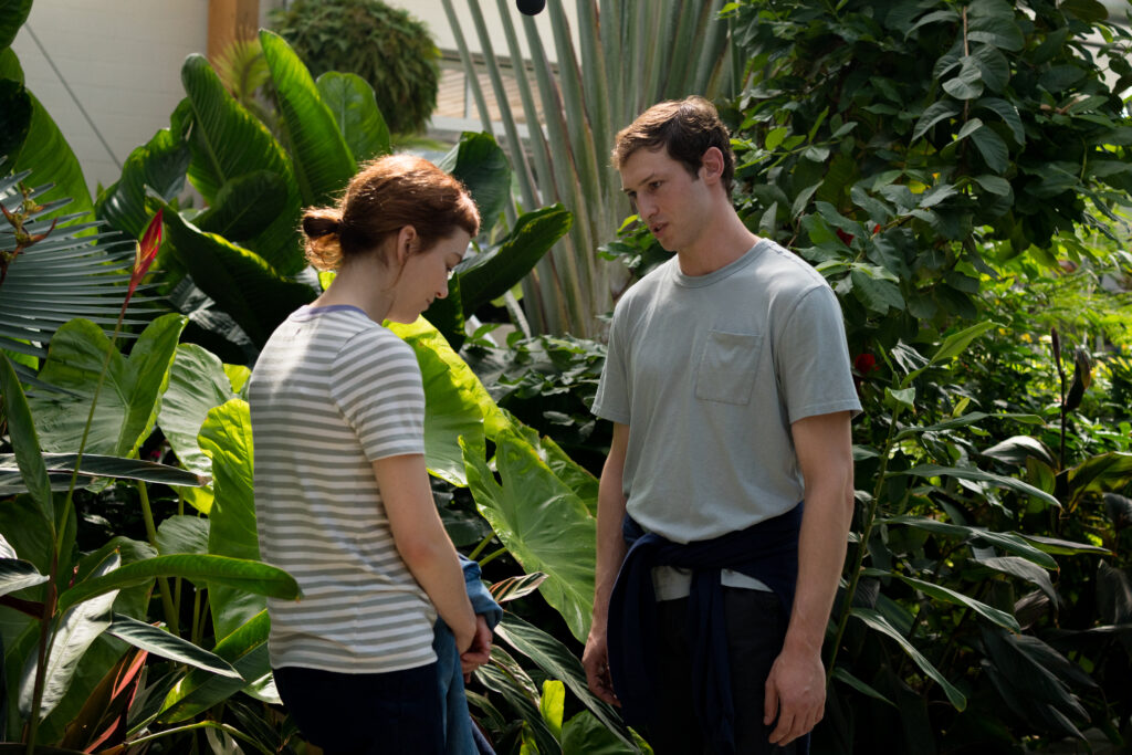 Britt Lower as Miriam walks with Tom Mercier as Janko standing talking awkwardly in botanical garden in the movie Darkest Miriam