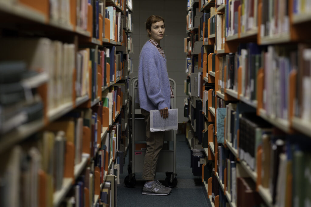 Britt Lower as Miriam looks back to camera as she stand in between book stacks in the library she works in in Darkest Miriam