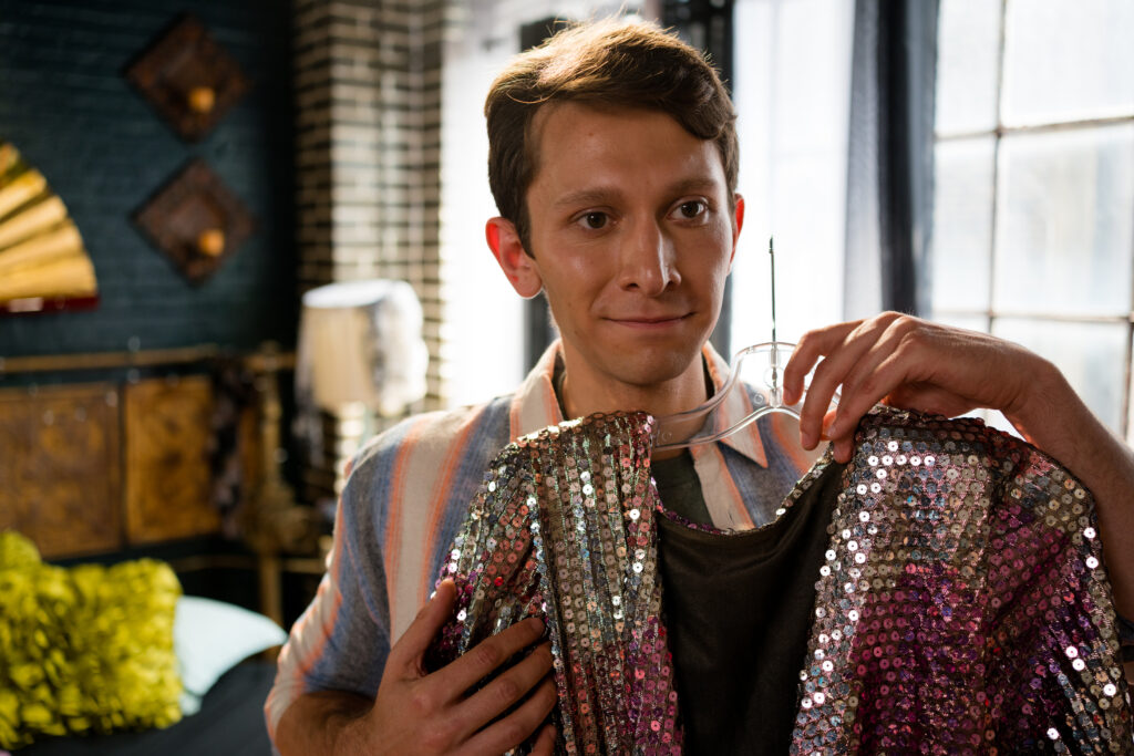 Ryan Ali looks at his reflection with a glittering dress in his hands