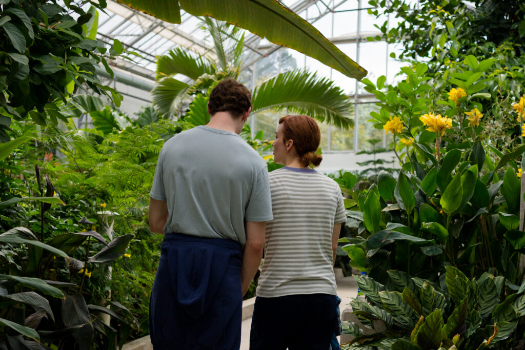 Britt Lower as Miriam walks with Tom Mercier as Janko walk together through a botanical garden in the movie Darkest Miriam