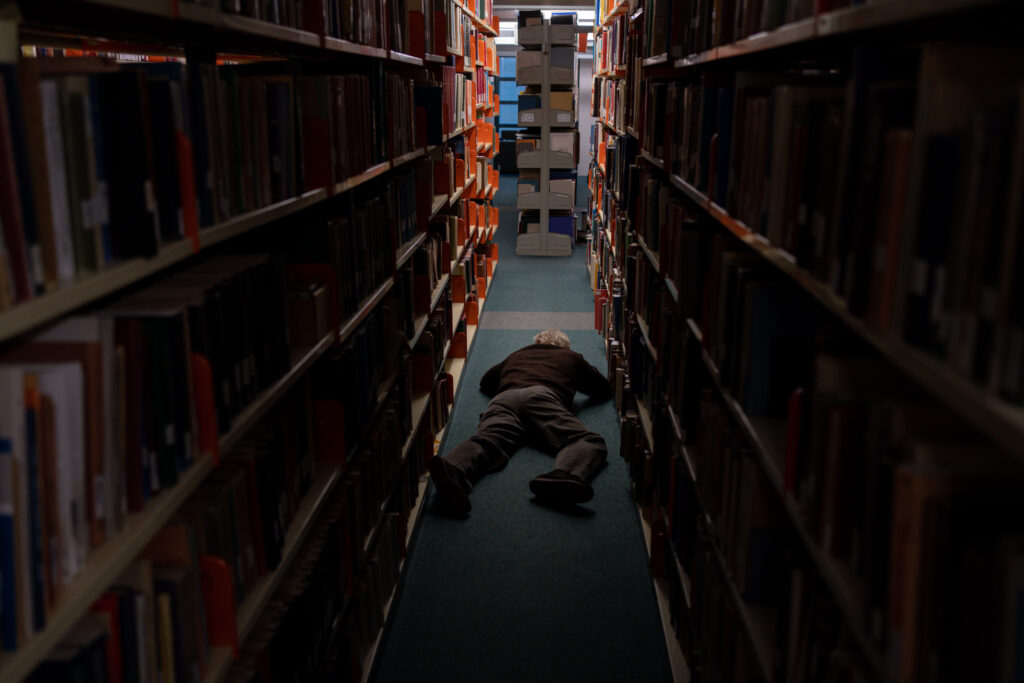 Man lies on floor in library in Film Darkest Miriam