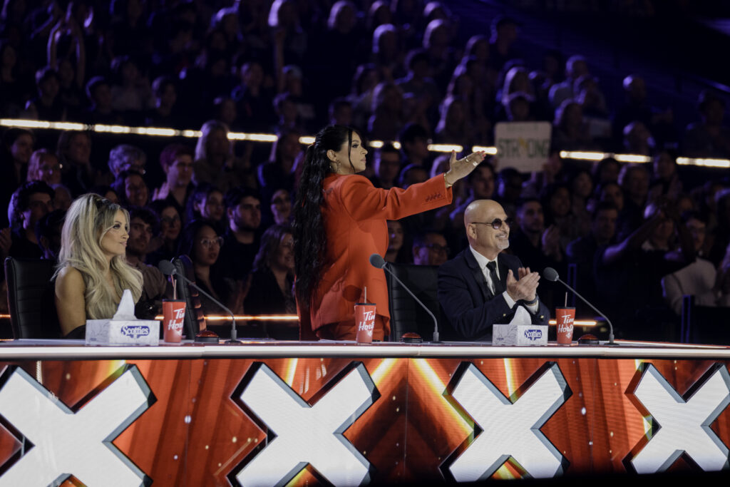 Judges of Canadas Got Talent sit and pose at judges desk with Howie Mandel, Lindsay Ell, Trish Stratus, Lilly Singh, Kardinal Offishall