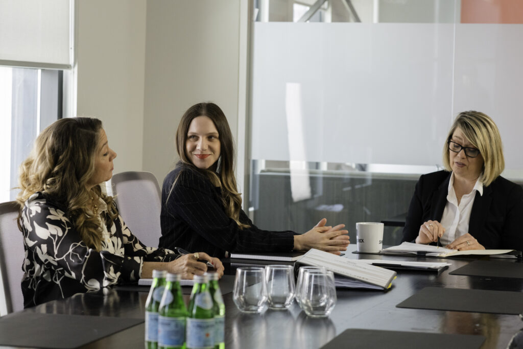Lauren Collins and Megan Follows in My Dead Mom talk at an office table at her work productivity meeting.