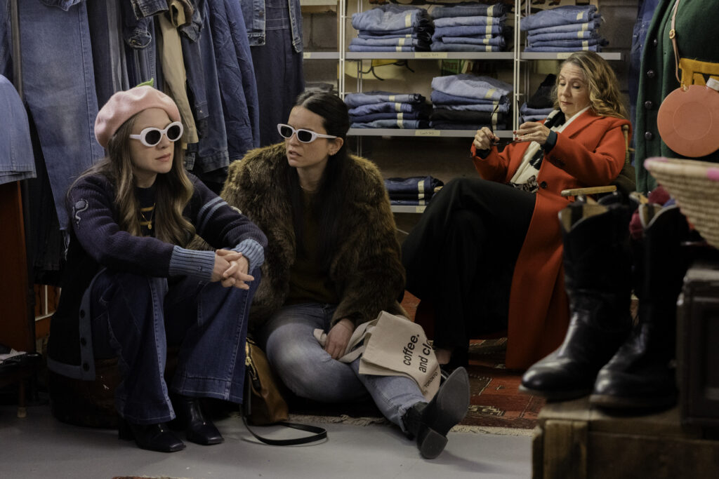 Lauren Collins, Jenny Raven and Megan Follows in My Dead Mom dressed in sunglasses and hats talk in a second hand store.