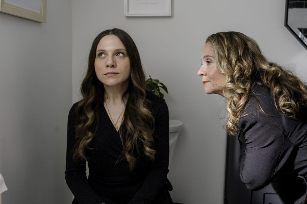 Lauren Collins and Megan Follows in My Dead Mom talk in bathroom.