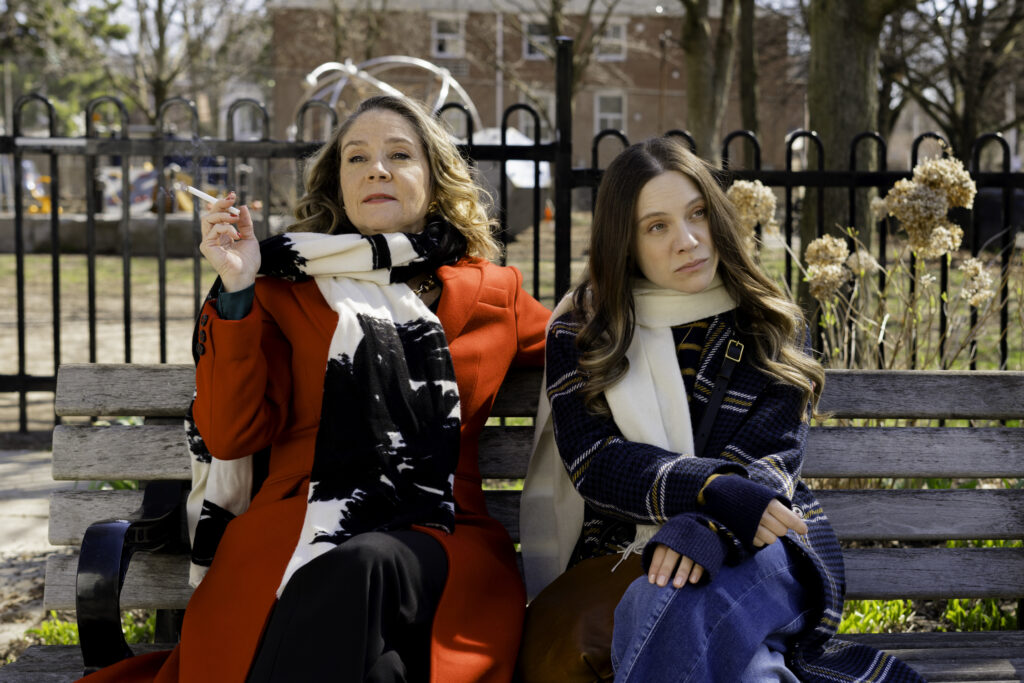 Lauren Collins and Megan Follows sit talking on a bench in My Dead Mom. Photo by Unit Stills Photographer Lauren Newman